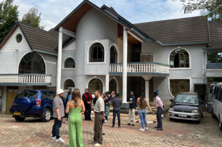 Two-story building shaped like a house and participants standing outsidew it looking at it