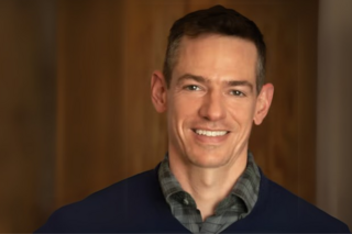 John Pachankis smiles in front of wood wall