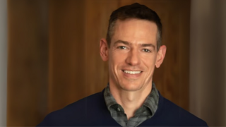 John Pachankis smiles in front of wood wall